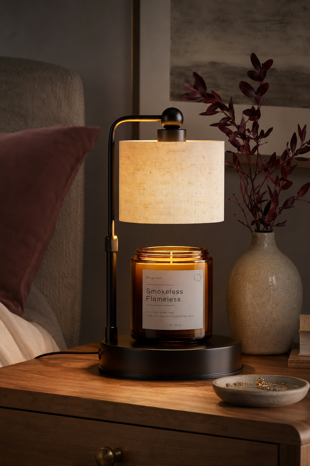 Black candle warmer lamp with cream shade and amber jar candle styled on a warm wood bedside table.