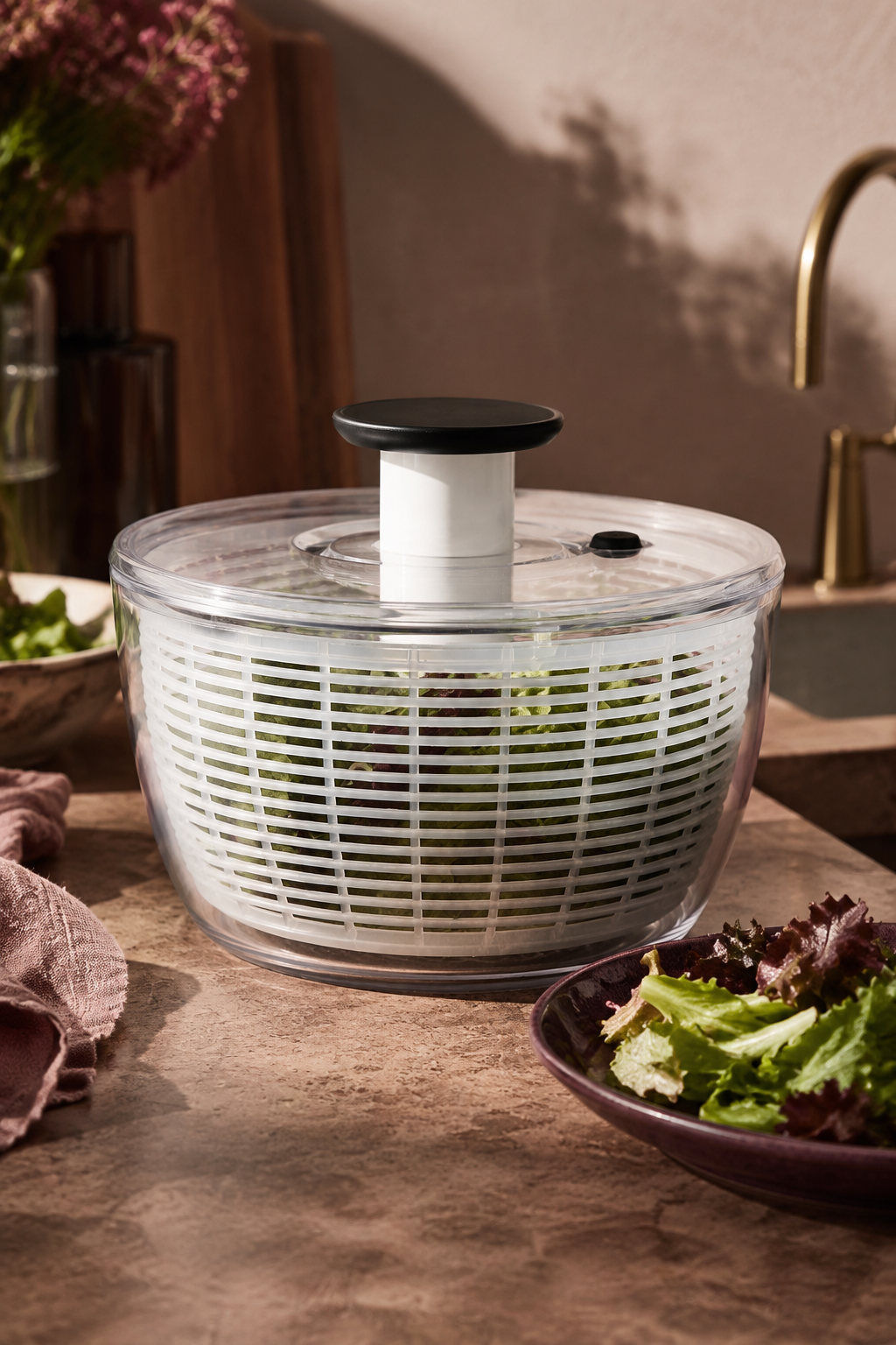 OXO Good Grips salad spinner filled with leafy greens on a warm kitchen prep counter.